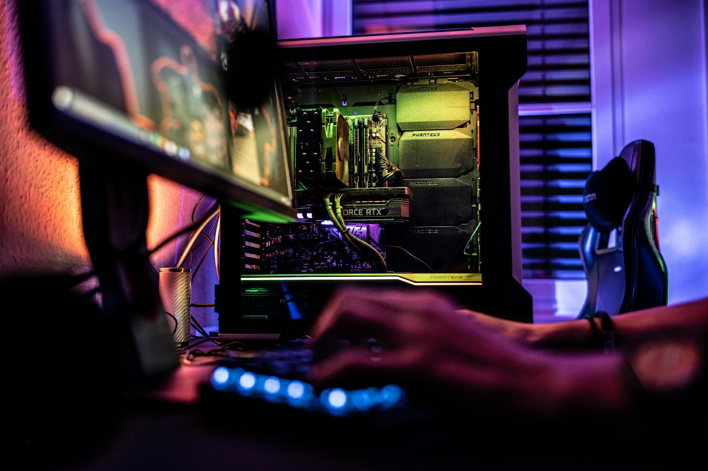 Hands typing on a glowing mechanical keyboard connected to a computer.
