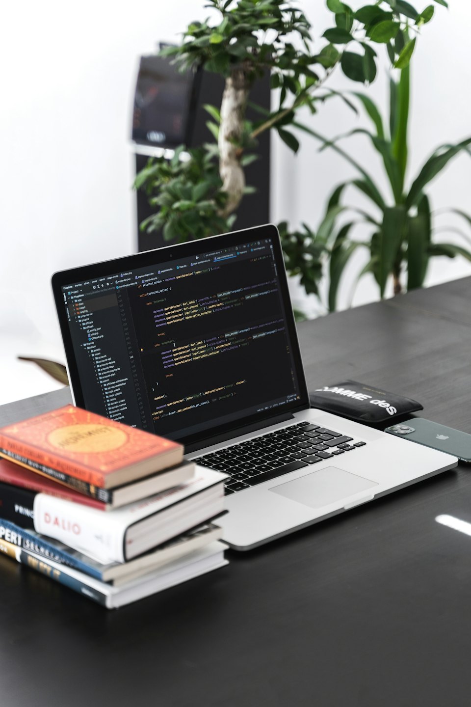 Laptop with programming code on a desk with books and phone.